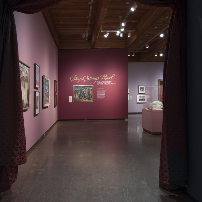 Maroon curtains frame the entrance to the exhibition, the walls inside are shades of burgundy and purple covered with paintings.