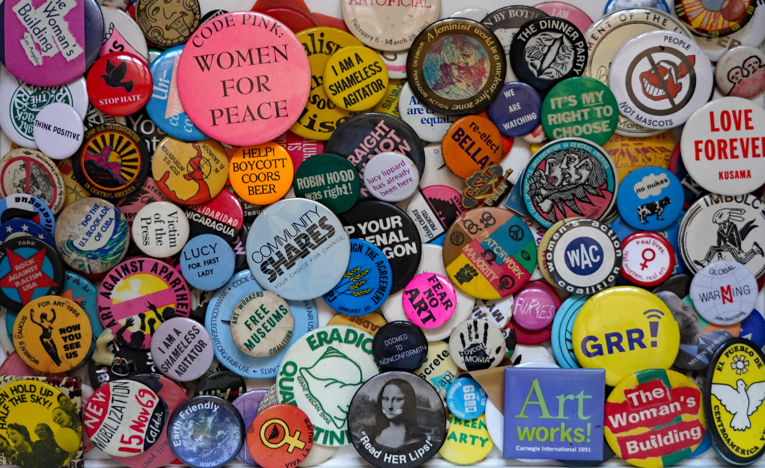 Numerous political buttons in a rainbow of colors overlap in a pile with some slogans visibile.