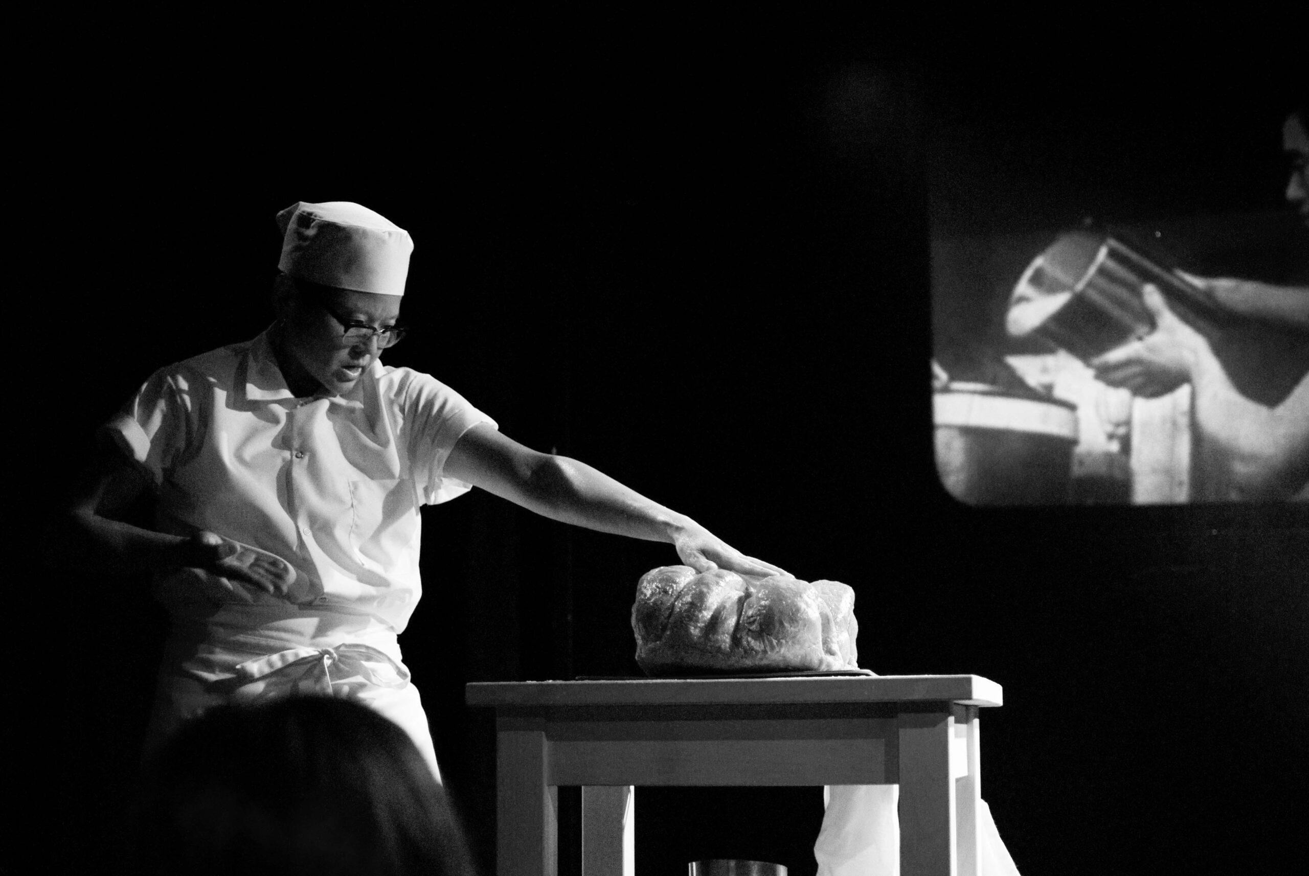 A black and white still from a video performance depicted a person in Japanese white chef linens