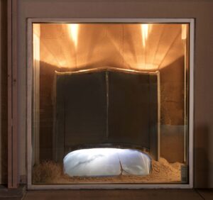 The front end of a car sticks up out of the ground. The windshield reflects a blue sky with white clouds.