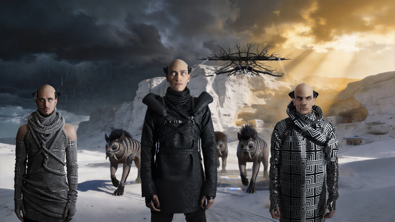 Three men in futuristic outfits stand in a desert landscape with three mythical creatures, as rain falls in the distance