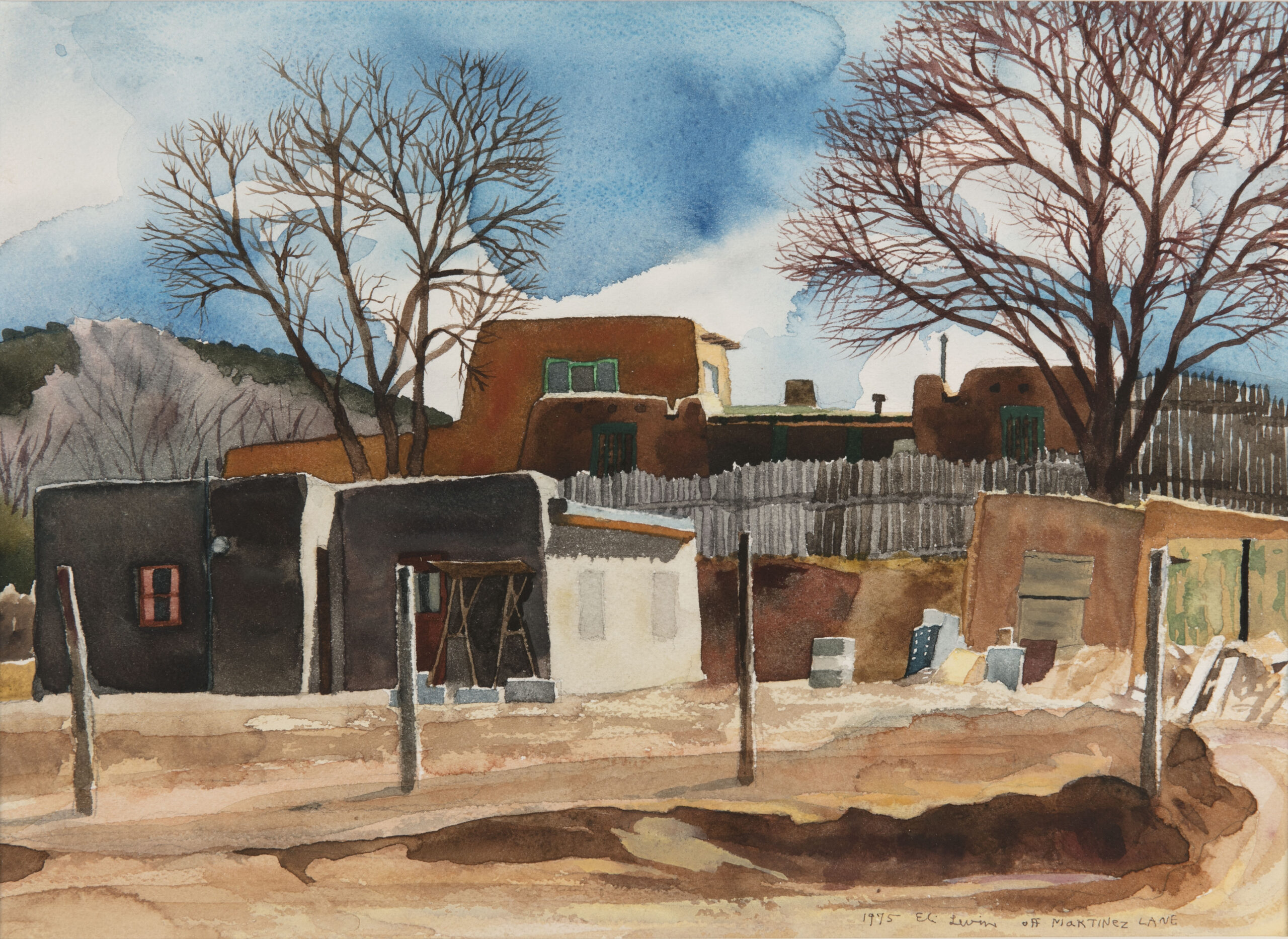 A watercolor painting depicting an adobe home and set of fence posts at a transitional season. Leaf-less tree branches stretch into the blue sky as shadows fall across the landscape of rugged earth.
